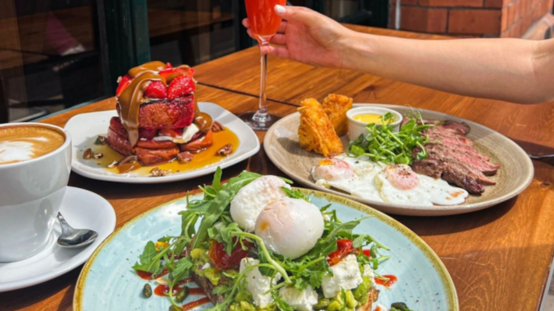 Someone holding a cocktail while sitting at a table with brunch dishes